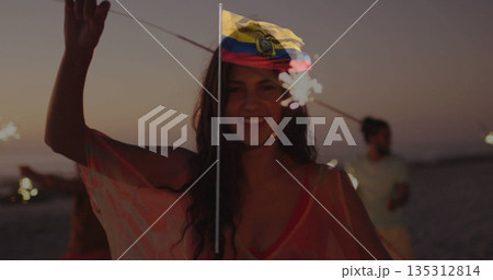Waving sparklers three friends on sandy shoreline at dusk, with translucent pink beach cover-up 135312814