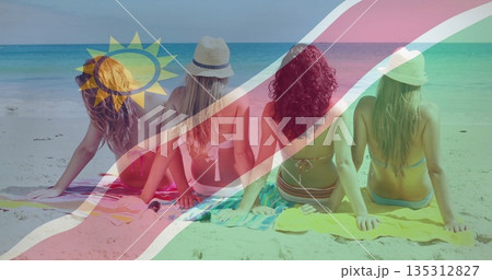 Wearing bright bikinis and sun hats, four friends sitting on towels at beach admiring turquoise sea 135312827