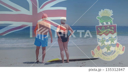 Gazing out senior couple standing on sandy shoreline, surfboard at feet with nautical flag overlay Gazing out senior couple standing on sandy shoreline, surfboard at feet with nautical flag overlay 135312847