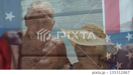 Smiling group of seniors in swimwear posing at beach shoreline, with straw sun hat, US flag 135312867