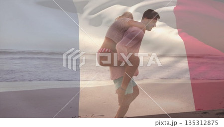 Piggybacking couple in swimwear walking along wet sand at beach edge, with French flag overlay 135312875