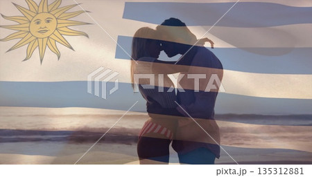 Embracing couple in swimwear and shirt hugging on beach at sunset, with Uruguay flag overlay Embracing couple in swimwear and shirt hugging on beach at sunset, with Uruguay flag overlay 135312881