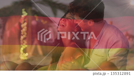 Laughing couple in linen shirt summer dress hugging on sandy beach at sunset, with string lights 135312891