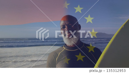 Standing man wearing wetsuit holding yellow surfboard at shore, with EU stars overlay Standing man wearing wetsuit holding yellow surfboard at shore, with EU stars overlay 135312953