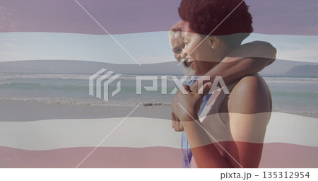 Embracing couple gazing toward horizon on sandy beach, with waves and pale blue sky, copy space Embracing couple gazing toward horizon on sandy beach, with waves and pale blue sky, copy space 135312954