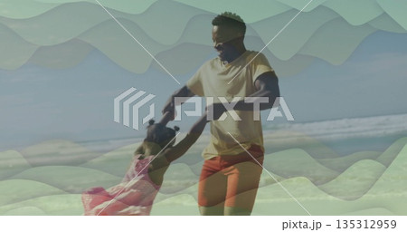 Spinning father wearing yellow tee and daughter in pink dress on sandy shoreline, with sunglasses 135312959