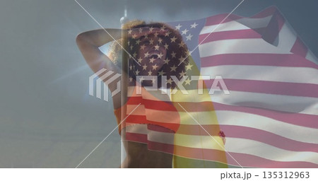 Standing woman wearing orange swim top under clear blue sky, with sun flare, American flag overlay 135312963