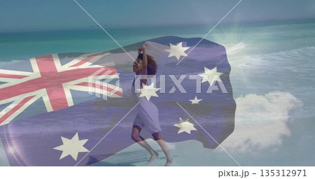 Running African woman wearing dress holding Australian flag in ocean waves on sandy beach, freedom 135312971