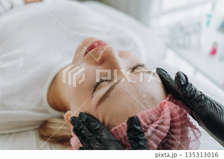 young woman getting professional face massage at aesthetic clinic 135313016