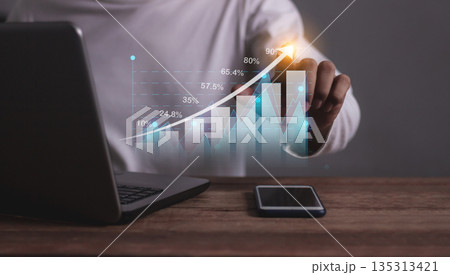 Young man with computer notebook and smartphone hand touching to visualize money growth The phone screen displays graphs and charts showing increasing investment and savings trends, along with an Young man with computer notebook and smartphone hand touching to visualize money growth The phone screen displays graphs and charts showing increasing investment and savings trends, along with an 135313421
