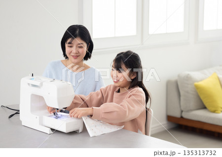 母親からミシンのかけ方を教わる小学生の女の子 母親からミシンのかけ方を教わる小学生の女の子 135313732