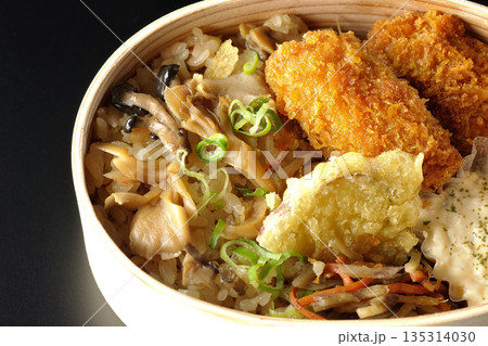 きのこご飯とカキフライ弁当を黒背景で撮影 135314030