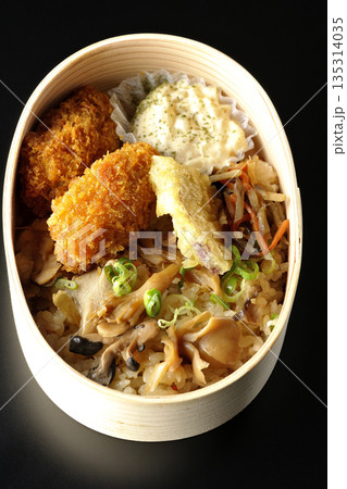 きのこご飯とカキフライ弁当を黒背景で撮影 135314035