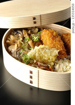 きのこご飯とカキフライ弁当を黒背景で撮影 135314050