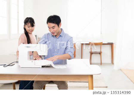小学生の娘の隣でミシンがけをする父親 小学生の娘の隣でミシンがけをする父親 135314390
