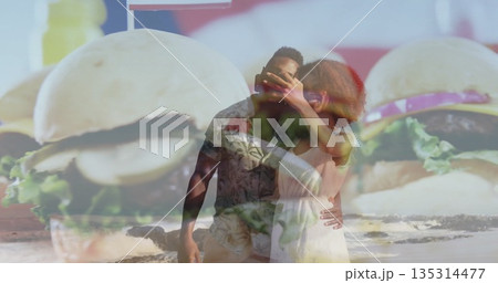 Embracing couple wearing dress and shirt and shorts standing on beach, giant burger billboard Embracing couple wearing dress and shirt and shorts standing on beach, giant burger billboard 135314477