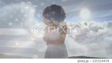 Standing woman wearing lace dress on misty hill, displaying semi-transparent American flag overlay Standing woman wearing lace dress on misty hill, displaying semi-transparent American flag overlay 135314478