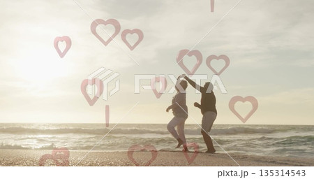 Dancing older couple twirling along beach shore at sunset, with heart-shaped overlays, copy space Dancing older couple twirling along beach shore at sunset, with heart-shaped overlays, copy space 135314543