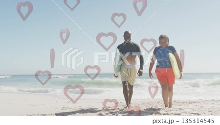 Walking mature man and senior woman surfers carrying surfboards on sandy beach near ocean waves 135314545