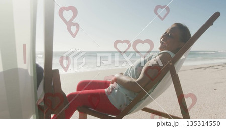Reclining woman wearing red leggings, blue top on beach in deck chair, heart graphics, copy space 135314550