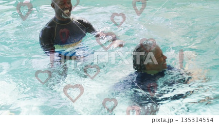 Laughing friends wearing dark swim tops interacting in therapy pool water, with heart-shaped decals Laughing friends wearing dark swim tops interacting in therapy pool water, with heart-shaped decals 135314554