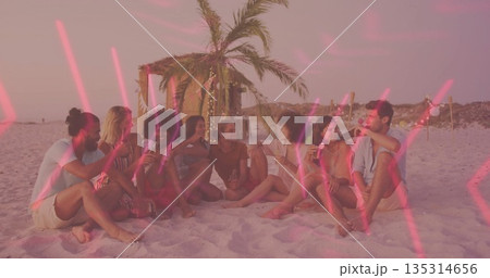 Group of eight friends clinking bottles and glasses on beach at sunset, with lit palm hut Group of eight friends clinking bottles and glasses on beach at sunset, with lit palm hut 135314656