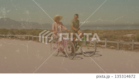 Riding couple on pink green cruisers along paved coastal path, wide-brimmed sun hat, low rail fence Riding couple on pink green cruisers along paved coastal path, wide-brimmed sun hat, low rail fence 135314672