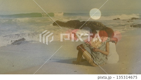 Sitting couple wearing tropical shirt and sundress hugging on sandy beach, with ocean waves Sitting couple wearing tropical shirt and sundress hugging on sandy beach, with ocean waves 135314675
