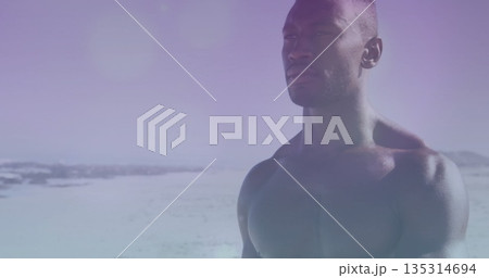 Standing shirtless muscular man wearing swim trunks at beach, gazing toward pastel sky, copy space Standing shirtless muscular man wearing swim trunks at beach, gazing toward pastel sky, copy space 135314694