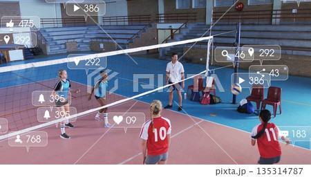 Competing players in blue and red jerseys spiking volleyball at school gym, with net, icons 135314787