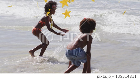 Splashing siblings diving in shallow ocean water at beach, with swim goggles and foamy waves 135314811