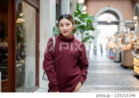 Young asian woman in knit sweater with bag standing and posing in hallway of shopping mall or market 135315146