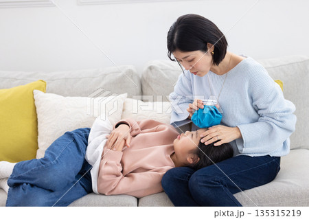 娘の額に氷嚢を当てる母親 135315219