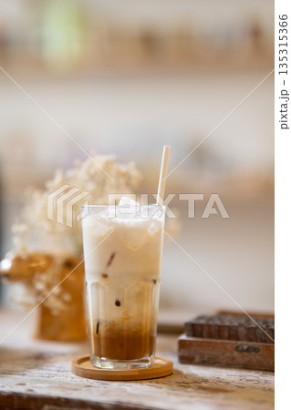 A glass of iced milk tea or coffee aside wooden blocks on working table in a pottery studio or cafe. 135315366