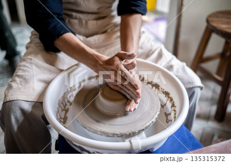 Close up of potter artist hands shaping clay into bowl on spinning throwing wheel in class or studio 135315372