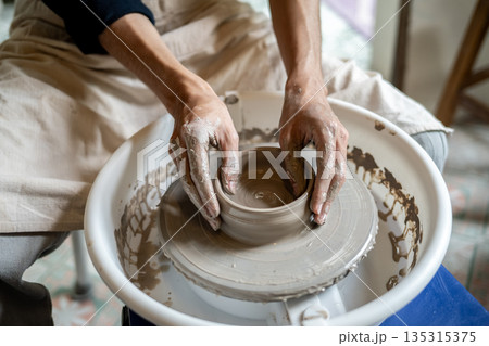 Close up of pottery artist's hands making a clay bowl on spinning throwing wheel in class or studio. Close up of pottery artist's hands making a clay bowl on spinning throwing wheel in class or studio. 135315375
