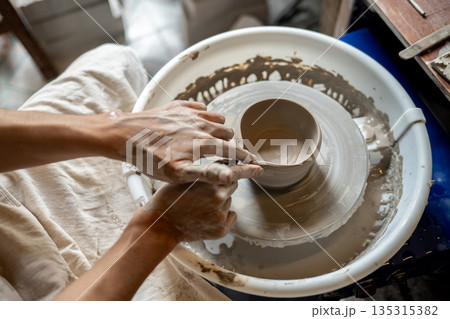 Pottery artist hand making clay into tea brewing bowl on spinning throwing wheel in class or studio. Pottery artist hand making clay into tea brewing bowl on spinning throwing wheel in class or studio. 135315382