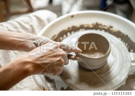 Close up pottery artist making a clay tea brewing bowl on spinning throwing wheel in class or studio Close up pottery artist making a clay tea brewing bowl on spinning throwing wheel in class or studio 135315383