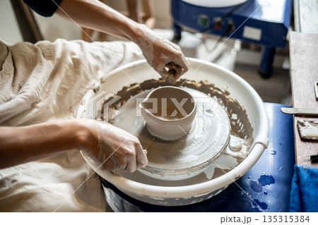 Close up pottery artist with a clay tea brewing bowl on spinning throwing wheel in class or studio 135315384