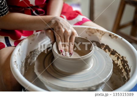 Painted nails pottery artist molding clay into a bowl on spinning throwing wheel in class or studio. 135315389