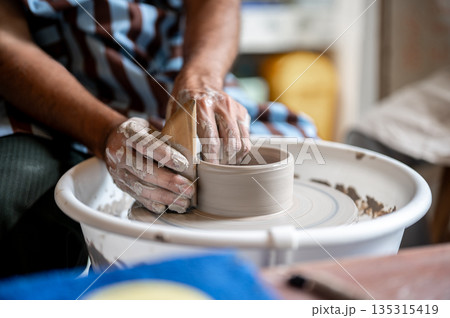 Close up pottery artist's hand using tool to smooth a clay bowl on throwing wheel in class or studio Close up pottery artist's hand using tool to smooth a clay bowl on throwing wheel in class or studio 135315419