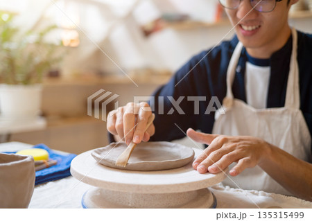 Potter artist glasses man molding clay to make a plate on working table in a pottery class or studio. 135315499