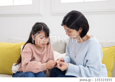 小学生の娘の指に絆創膏を貼る母親 小学生の娘の指に絆創膏を貼る母親 135315935