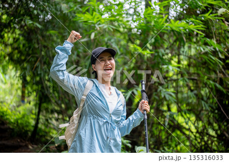 Happy asian tourist woman standing holding trekking cane and raising fist on a solo hiking in forest Happy asian tourist woman standing holding trekking cane and raising fist on a solo hiking in forest 135316033