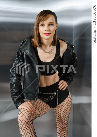 Woman poses confidently in black outfit near shiny silver backdrop during photo shoot Woman poses confidently in black outfit near shiny silver backdrop during photo shoot 135316076