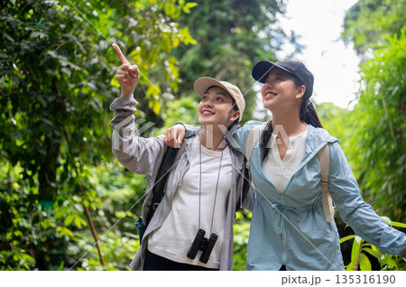 Backpacker tourist woman friends with binoculars looking pointing while hiking or trekking in forest Backpacker tourist woman friends with binoculars looking pointing while hiking or trekking in forest 135316190