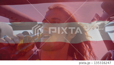Raising male passenger drinking from brown glass bottle in convertible car, wind blowing hair back 135316247