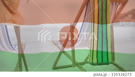 Displaying striped deck chairs positioned on sandy beach by calm sea, with straw hat and towel Displaying striped deck chairs positioned on sandy beach by calm sea, with straw hat and towel 135316273