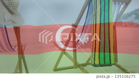 Wooden folding chairs facing sea on beach with pastel-striped seats, striped towel, straw sun-hat 135316275