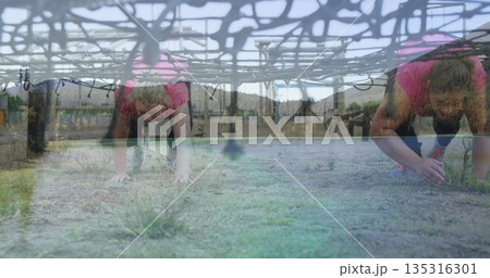 Crawling women wearing pink tops and leggings under rope net at obstacle course, with wooden posts Crawling women wearing pink tops and leggings under rope net at obstacle course, with wooden posts 135316301
